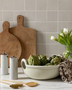 an assortment of artichokes in a bowl on a counter next to cutting boards and utensils