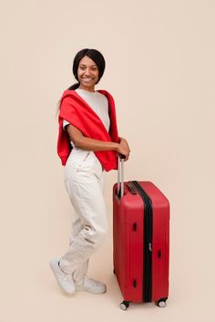 a woman standing next to a red piece of luggage with her hands on the handle