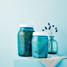 two jars filled with green beans sitting on top of a blue tablecloth next to flowers