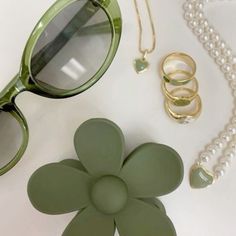 a pair of green sunglasses, pearl necklace and flower brooch on a white surface