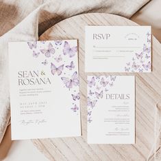 the wedding stationery is laid out on a wooden table with purple and white butterflies