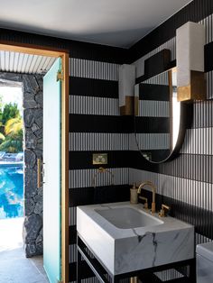 a bathroom with black and white wallpaper, gold faucet, marble sink and mirror