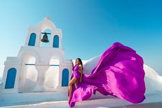 a woman in a purple dress standing next to a bell tower