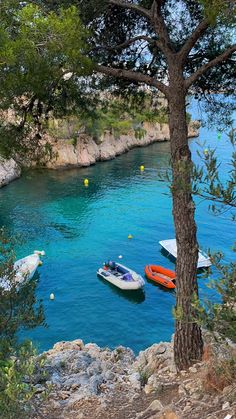 three boats floating in the blue water next to a rocky shore with trees on either side