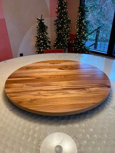 a large wooden board on top of a round table with christmas trees in the background