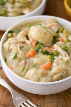 two white bowls filled with chicken and dumplings on top of a wooden cutting board