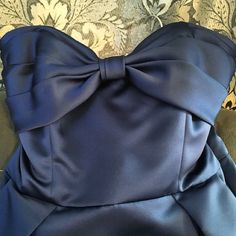 the back of a blue dress with a large bow on it's shoulder, sitting on a couch