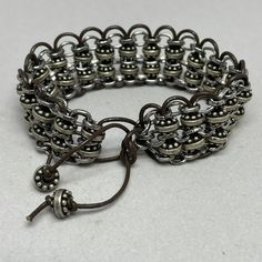 Woven bracelet, silver chain and beads woven with dark brown leather cord.  Is adjustable 7 inches to 9.5 inches.   The bracelet is 3/4 inch wide.  Reminiscent of chain mail.  To see more unique creations, click here: https://KingBlazCreations.etsy.com I take great pride in providing exceptional quality and service!  My top priority is your satisfaction of the design you've ordered.  I want you to love your jewelry as much as I loved creating it.  Please contact me if your expectations are not m Adjustable Gunmetal Metal Bracelet, Adjustable Gunmetal Metal Bracelets, Handmade Adjustable Metal Braided Bracelets, Adjustable Handmade Metal Braided Bracelet, Brown Metal Beaded Bracelets With Round Beads, Adjustable Silver Metal Braided Bracelet, Brown Metal Beaded Bracelets As Gift, Brown Metal Beaded Bracelets For Gifts, Brown Metal Beaded Bracelets