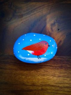 a painted rock with a red bird on it sitting on top of a wooden table