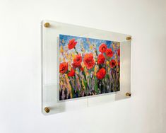 an acrylic painting of red poppies hangs on a white wall with brass brackets