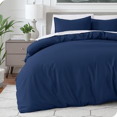 a bed with blue sheets and pillows in a room next to a potted plant