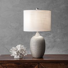 a white vase sitting on top of a wooden table next to a lamp and flowers