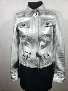 Stylish women's silver leather jacket. Solid silver women's leather jacket with belt. The jacket is made of durable silver-colored genuine leather. The jacket is easily fastened with a metal zipper, which is covered with a leather strip on the snaps, and is tied with a leather belt. The jacket has two convenient pockets at the bottom and two pockets at the top with flaps, as well as a small pocket on the left side on the zipper. The cuffs of the jacket are fastened with metal buttons. The jacket has a lovely polyester lining with lovely prints. The jacket is stylish and reliable to wear. the jacket has a stylish cut with reliable elements that will emphasize your independence, confidence and mystery. MEASUREMENTS Jacket length                  52 cm  |  20.5 in Pit to pit Leather Jacket With Belt, Silver Leather Jacket, Fitted Biker Jacket, Womens Leather Biker Jacket, Women Leather Vest, Black Leather Motorcycle Jacket, Motorcycle Jacket Women, Biker Pants, Sheepskin Coat