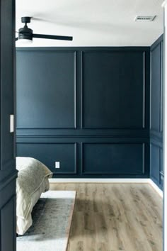 an empty bedroom with dark blue walls and wood flooring is seen from the doorway