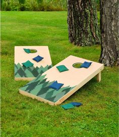 two cornhole boards sitting in the grass next to a tree with blue pillows on them