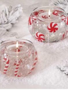 two glass candles sitting on top of snow next to pine cones and candy canes