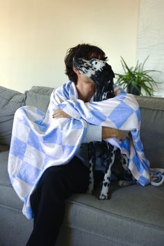 a woman wrapped in a blue and white checkered blanket sitting on a couch with her dog