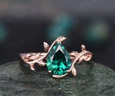 a green stone ring sitting on top of a piece of rock with leaves around it