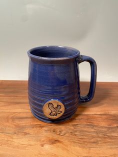 a blue ceramic mug with a wooden emblem on the side sitting on a wood table