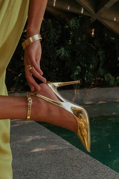 We seriously can't imagine a night out without a party-starting look like the D'Amelio Footwear Kamila Gold Specchio Metallic Ankle Strap Pumps! Strut your stuff in the most glamorous way with these shiny, faux patent leather pumps that feature a classic pointed-toe upper that carries into slender straps that wrap and secure around the ankle with a matching gold buckle. A sexy stiletto heel makes this sleek silhouette even more stunning. 4" wrapped stiletto heel. Cushioned insole. Rubber sole ha Gold Womens Shoes, Classy Women Shoes, Golden Heels Aesthetic, Gold Strapped Heels, Gold Shoes Aesthetic, Gold Pointed Toe Heels, Elegant Shoes Heels Classy, Gold Rhinestone Heels, Gold Heels Aesthetic