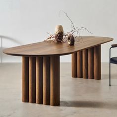 a wooden table sitting on top of a white floor next to a chair and vase