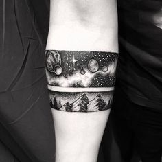 a black and white photo of a man's arm with mountains, stars and planets on it