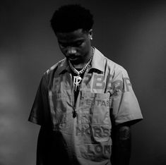 a man standing in front of a dark background wearing a shirt with letters on it