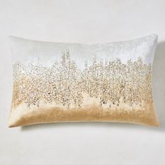 a gold and white pillow with metallic foil on the front, sitting against a wall