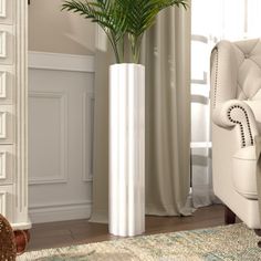 a tall white vase sitting on top of a rug next to a chair and potted plant