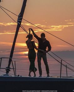 two people standing on the deck of a boat at sunset with their arms in the air