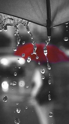 black and white photograph of an umbrella with water droplets on the outside, red umbrella in background