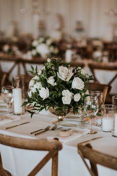 the centerpieces on this table are white roses and greenery, with candles in them