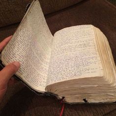 an open book with writing on it being held up by someone's hand while sitting on a couch