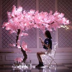 a woman sitting in a chair under a pink tree