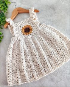 a white crocheted dress with a sunflower on the front, and a wooden hanger next to it