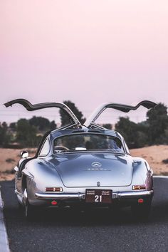 an old silver sports car driving down the road