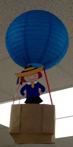 a paper bag with a woman holding a blue balloon on it's head hanging from the ceiling