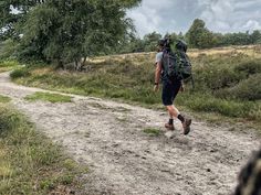 a man walking down a dirt road with a backpack on his back and trees in the background