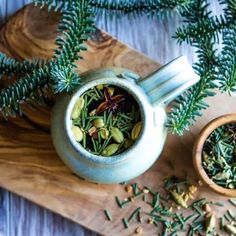 a tea pot filled with green herbs next to a wooden bowl full of leaves and seeds