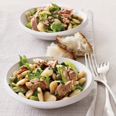 a white bowl filled with pasta and meat on top of a table next to bread