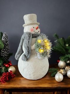 a snowman is sitting on top of a wooden table with christmas decorations around it