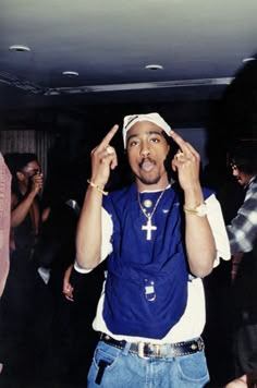 a man standing in front of a crowd holding his hands up to his face and making the peace sign