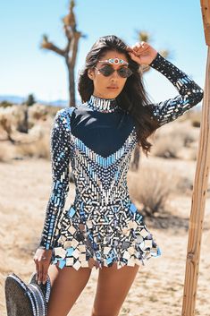 a woman is posing in the desert wearing a dress and hat with her hands on her head