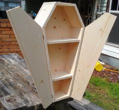 an unfinished cabinet sitting on top of a wooden table next to a brick wall and grass