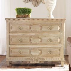 a white dresser sitting in a living room next to a chair and potted plant