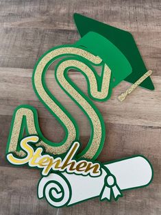 a green and gold graduation hat sitting on top of a wooden table next to a sticker