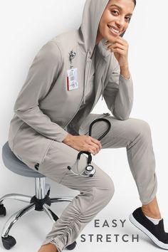 Female medical professional sitting on a stool wearing the Easy STRETCH by Butter-Soft™ Halle Women's 9-Pocket Ruched Leg Jogger Scrub Pants and Selena Women's 5-Pocket Long Sleeve Zip-Front Scrub Hoodie Grey Scrubs Aesthetic, Women’s Scrubs, Scrub Pants Outfit, Trendy Scrubs, Scrubs Shirt, Style Uniform, Scrubs Outfit