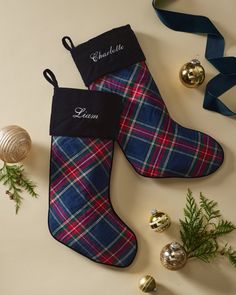 two christmas stockings sitting next to ornaments on a white table with blue ribbon and name tag