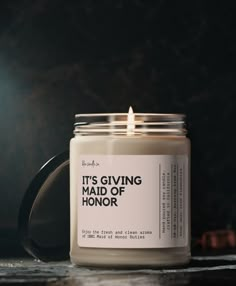 a candle that reads it's giving maid of honor in front of a dark background