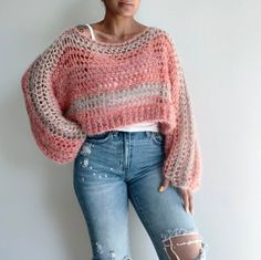 a woman standing in front of a white wall wearing ripped jeans and a pink sweater